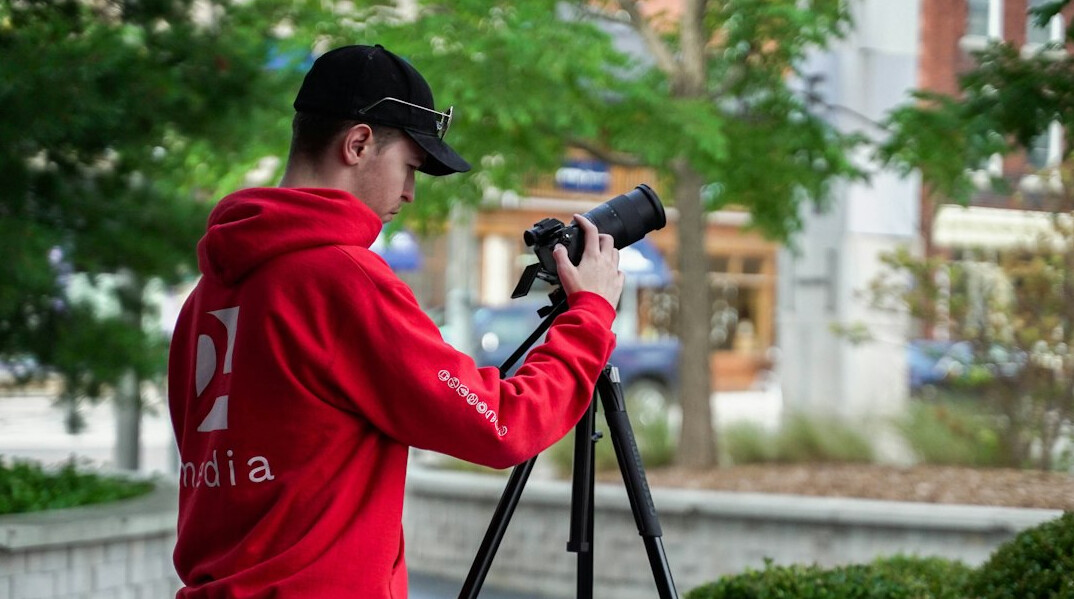 Camera operator adjusting a broadcast camera on a tripod outdoors